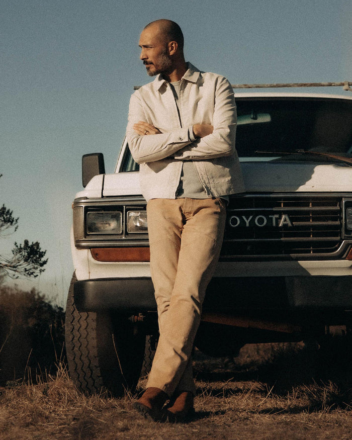 fit model leaning against a car wearing The Shifter Jacket in Stone Pigment Canvas