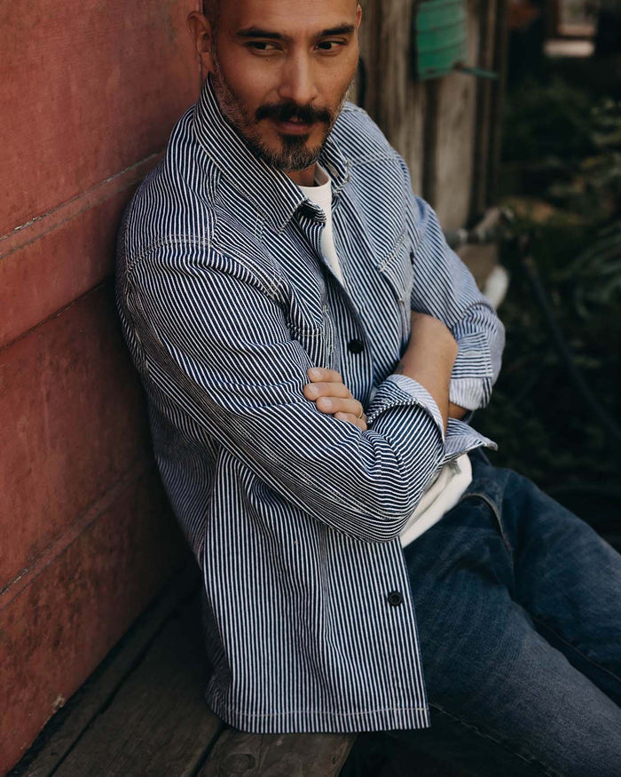 fit model sitting against the wall wearing The Shop Shirt in Rinsed Indigo Selvedge