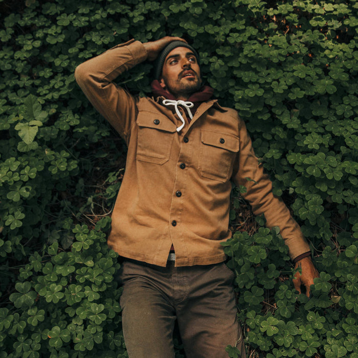 fit model wearing The Shop Shirt in Tobacco Boss Duck, laying in clovers