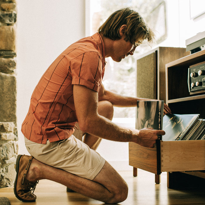 fit model looking through records in The Short Sleeve Hawthorne in Rust Stripe