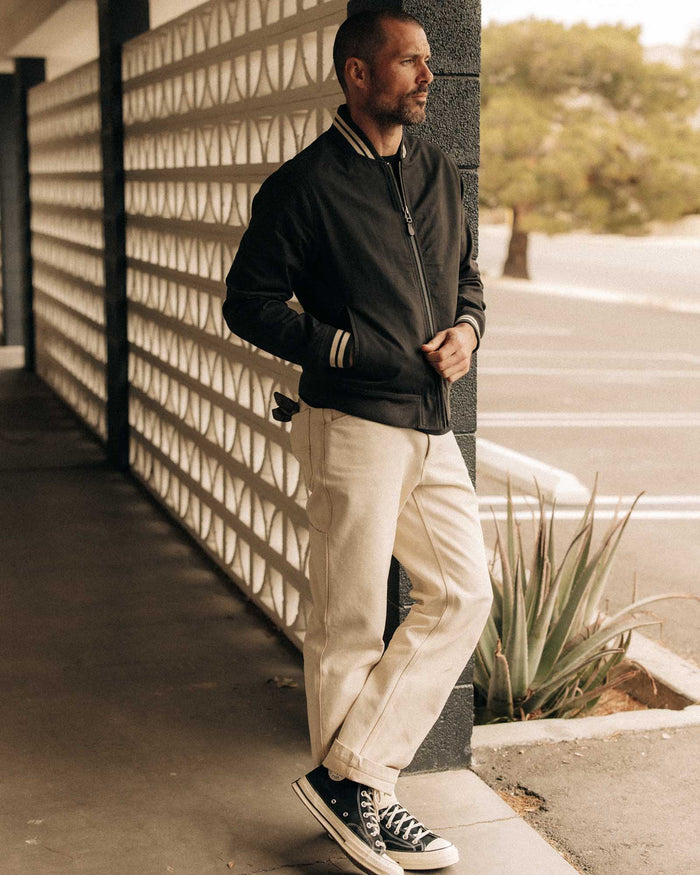 fit model leaning against the wall wearing The Speedway Bomber in Organic Faded Black Twill
