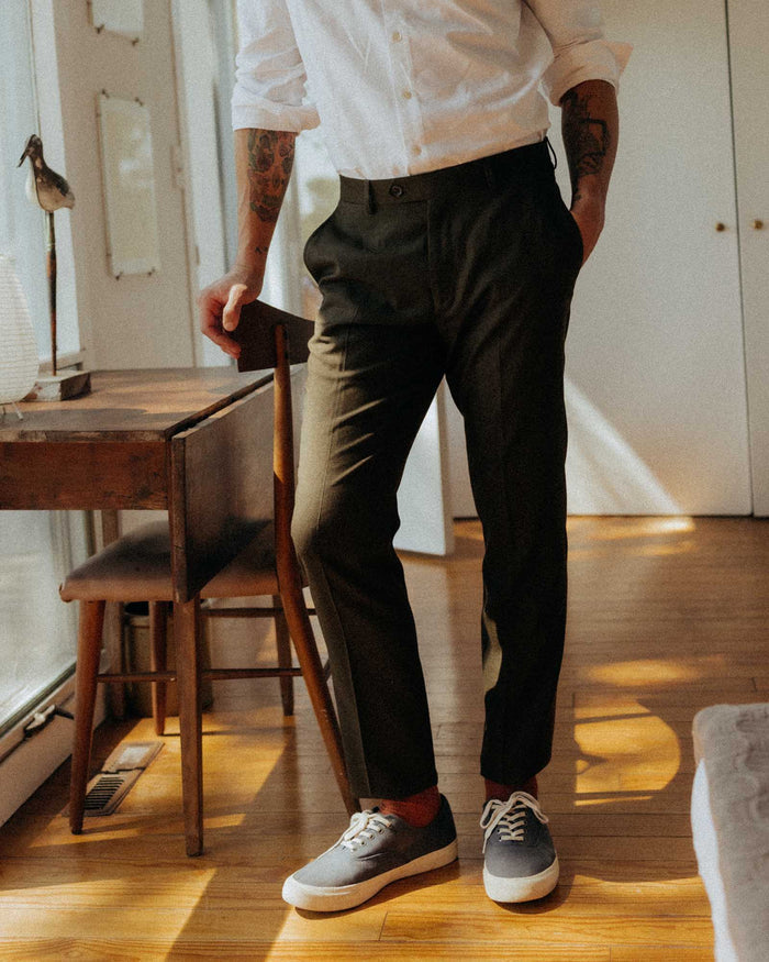fit model leaning against a chair wearing The Stevens Trouser in Black Olive Wool Flannel