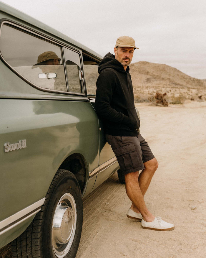 fit model leaning against a car wearing The Apres Hoodie in Black Indigo Terry