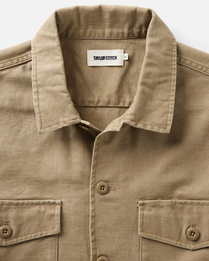 fit model leaning against the wall wearing The Surplus Shirt in Khaki Reverse Sateen