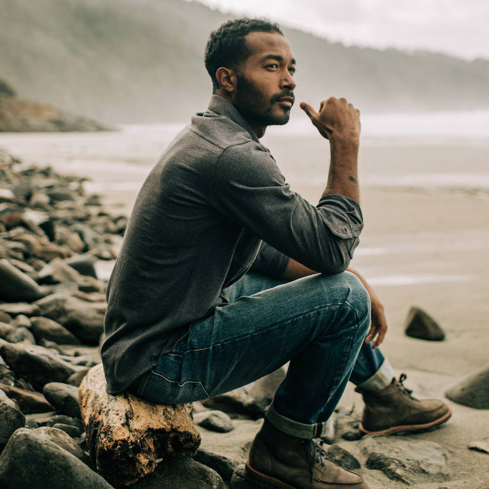 fit model sitting on a log in The Utility Shirt in Dark Charcoal Heavy Bag
