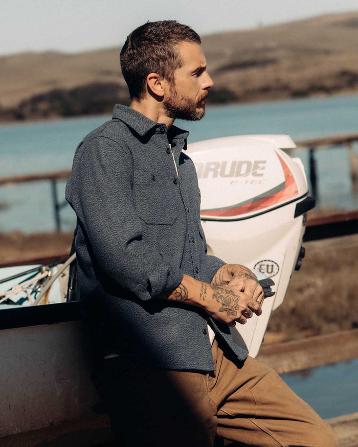 fit model leaning against a boat wearing The Utility Shirt in Indigo Ash Wool Canvas