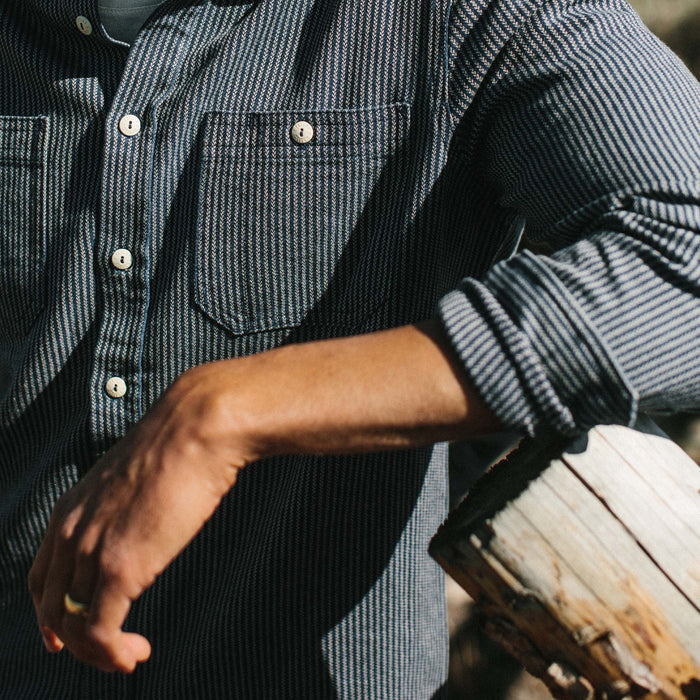 Fit model wearing The Utility Shirt in Roped Indigo leaning against a fence pole