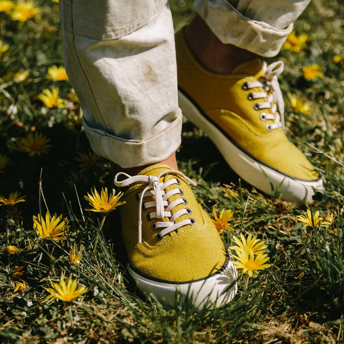 fit model wearing The Vista Sneaker in Gold Boss Duck, standing in grass