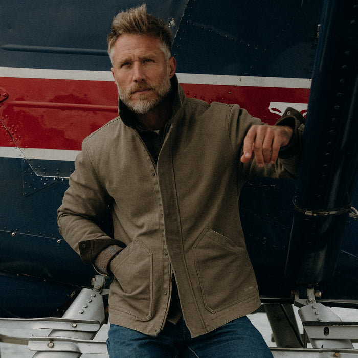 fit model posing on a seaplane wearing The Workhorse Jacket in Stone Chipped Canvas