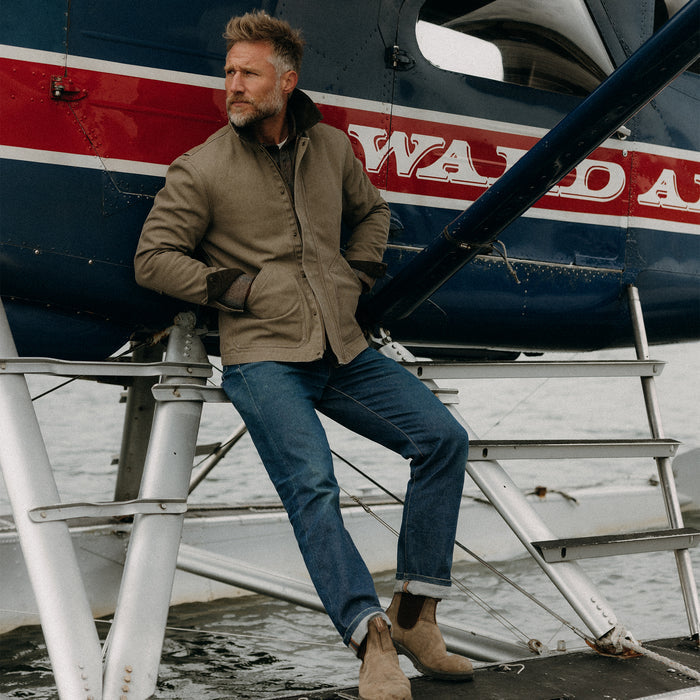 fit model sitting on a seaplane wearing The Workhorse Jacket in Stone Chipped Canvas