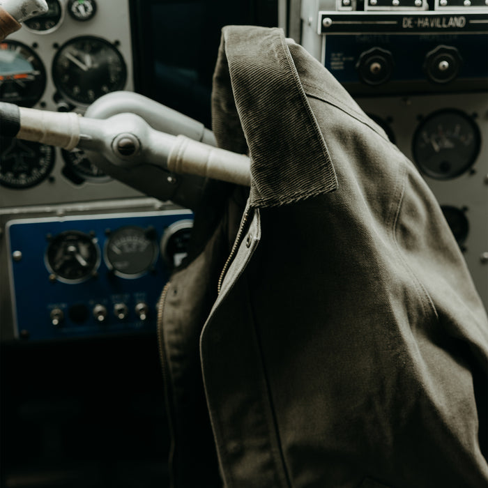 editorial image of The Workhorse Jacket in Stone Chipped Canvas hanging off of a seaplane wheel