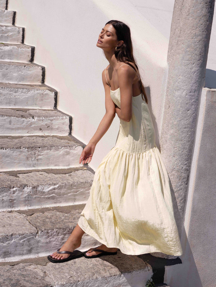 Woman in a light yellow dress standing on stone steps with a white wall background